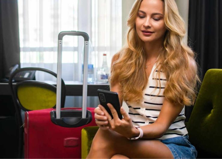 Turista con valigia rossa prenota bnb da smartphone