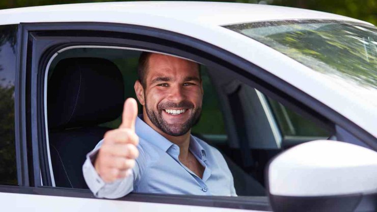 Uomo felice in auto fa segno con il pollice in su